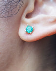 Close-up of an ear wearing a 14k yellow gold emerald stud round cut earring.