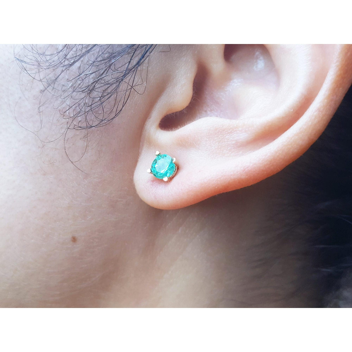 Close-up of an earlobe wearing a round cut emerald stud earring.