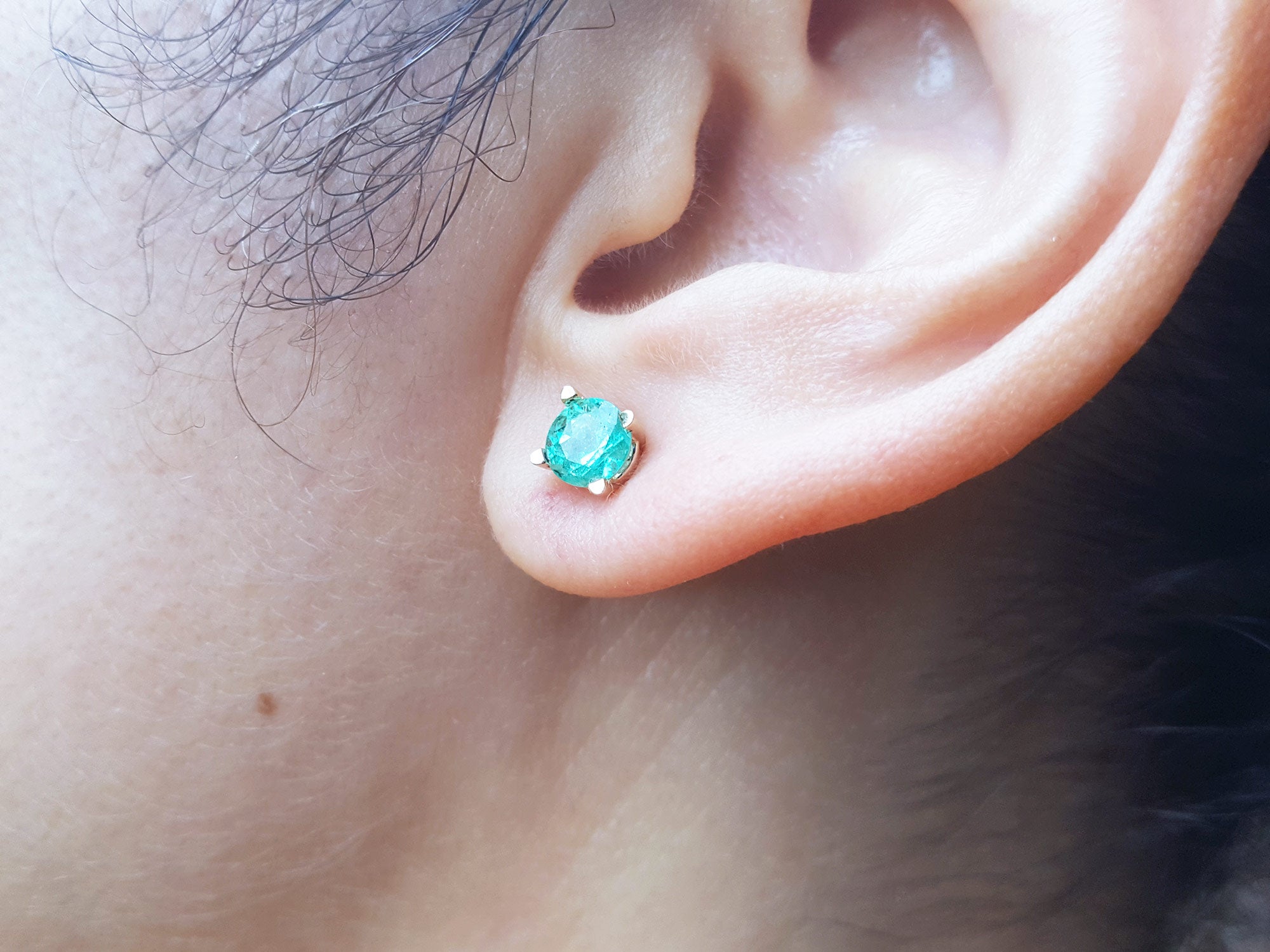 Close-up of an earlobe wearing a round cut emerald stud earring.
