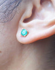 Close-up of an earlobe wearing a round cut emerald stud earring.