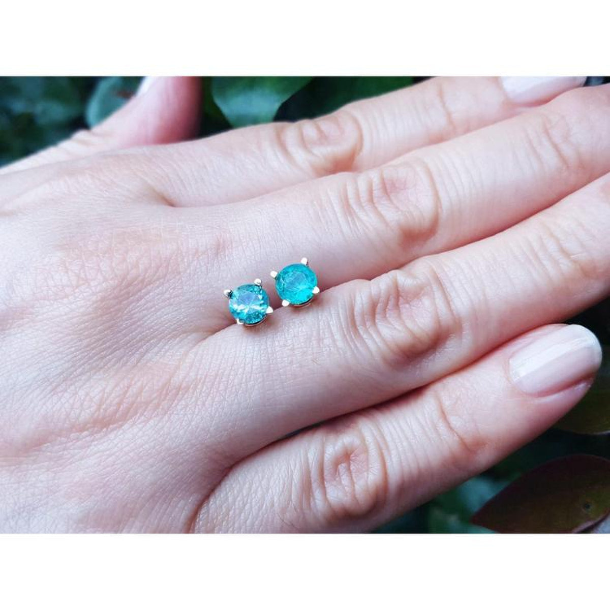 1.09 ct. natural Colombian emerald stud earrings in 14K gold basket settings with push backs, displayed on a hand.