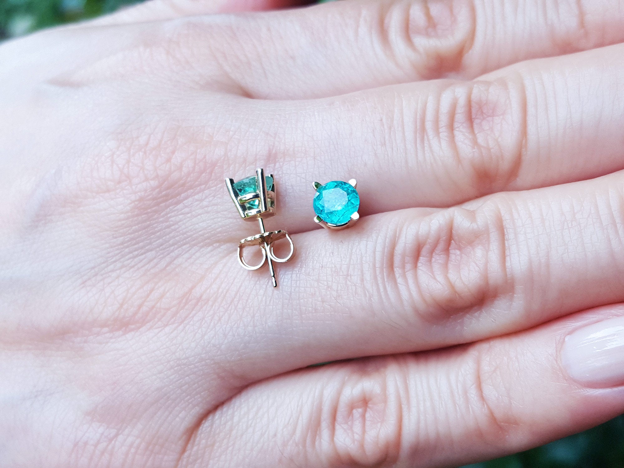 A pair of 14k yellow gold emerald stud earrings round cut and push backs on a hand.