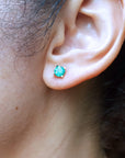 Close-up of a woman's ear wearing a 14k yellow gold emerald round cut stud earring.