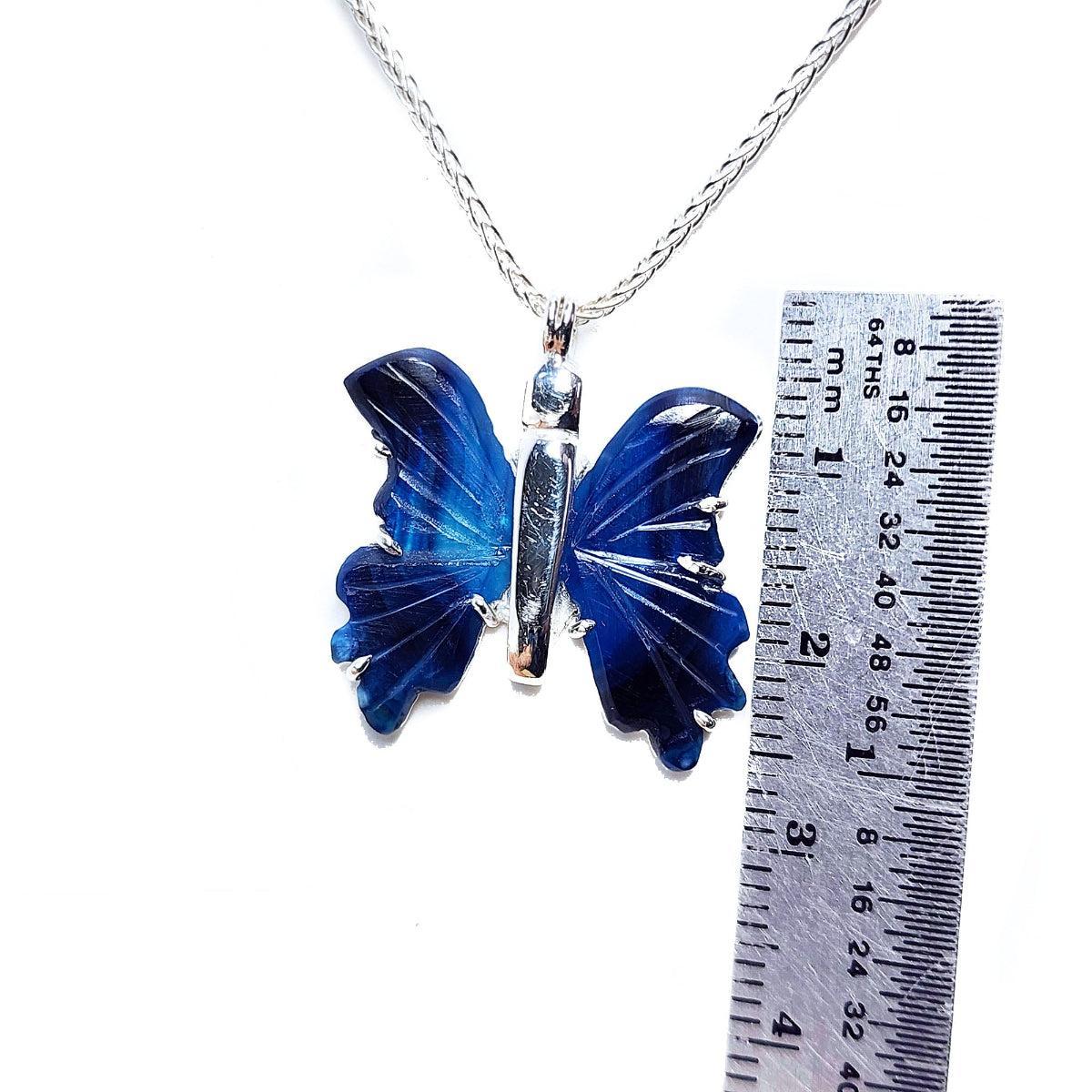 Blue agate butterfly pendant on a chain with a ruler for scale on a white background