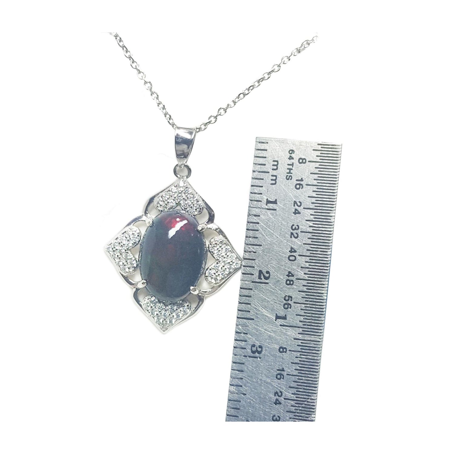 Jewelry pendant with a black opal and silver accents, next to a ruler for scale on a white background