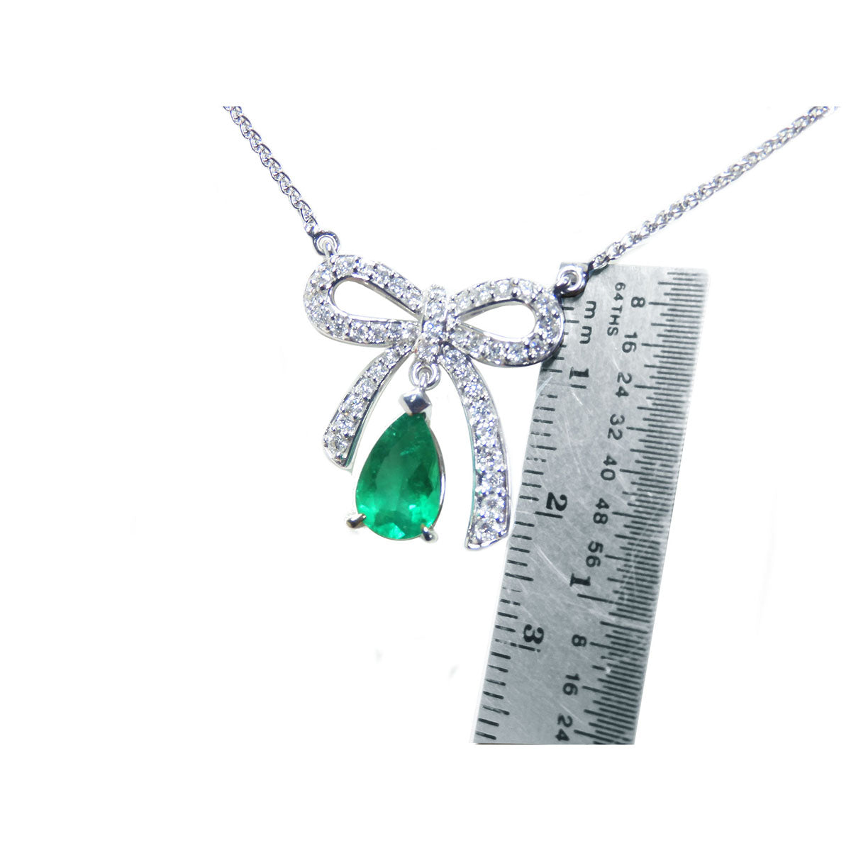 Necklace with a bow and emerald pendant next to a ruler for scale on a white background