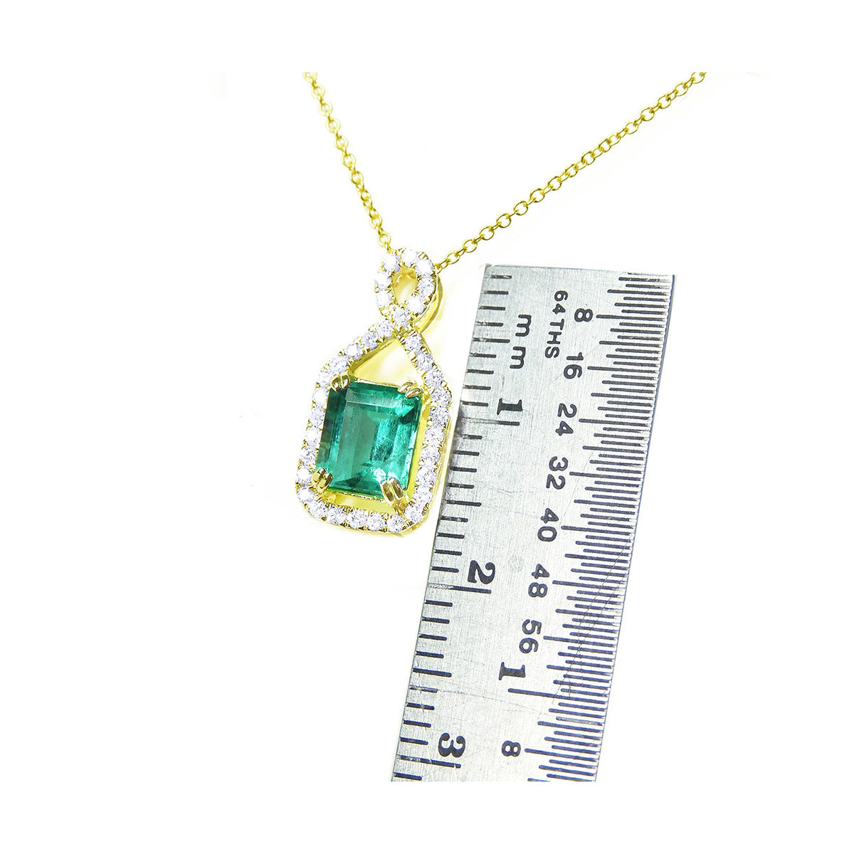 Gold necklace with a natural emerald gemstone pendant next to a ruler for scale on a white background