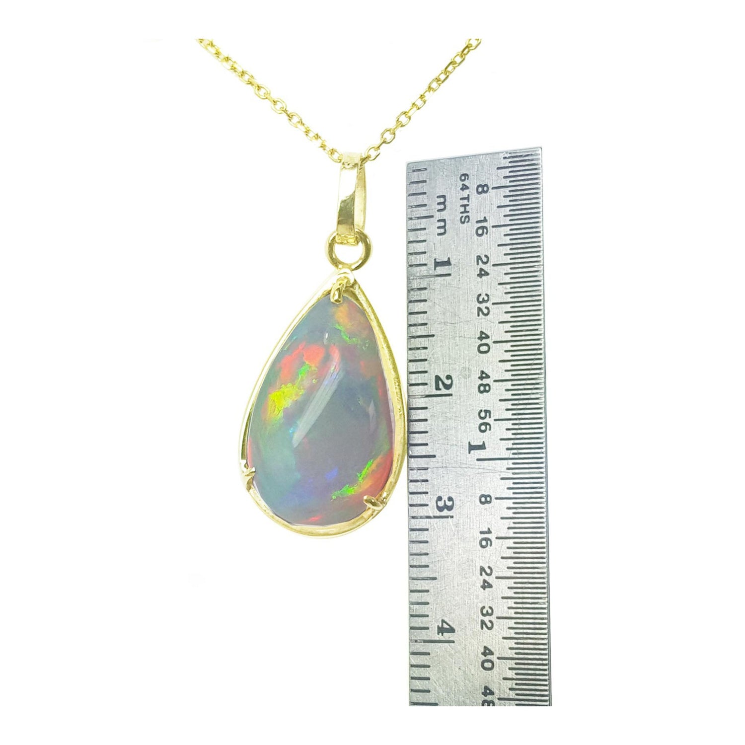 Opal pendant on a gold chain with a ruler for scale on a white background