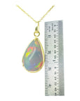 Opal pendant on a gold chain with a ruler for scale on a white background