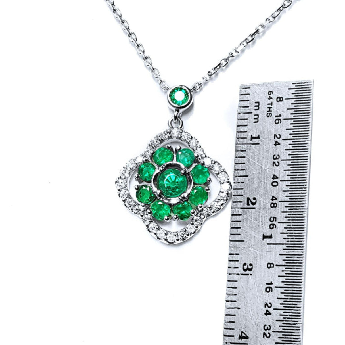 Green, emerald cluster pendant necklace 4-leaf clover design accented by natural diamonds with a ruler for scale on a white background 