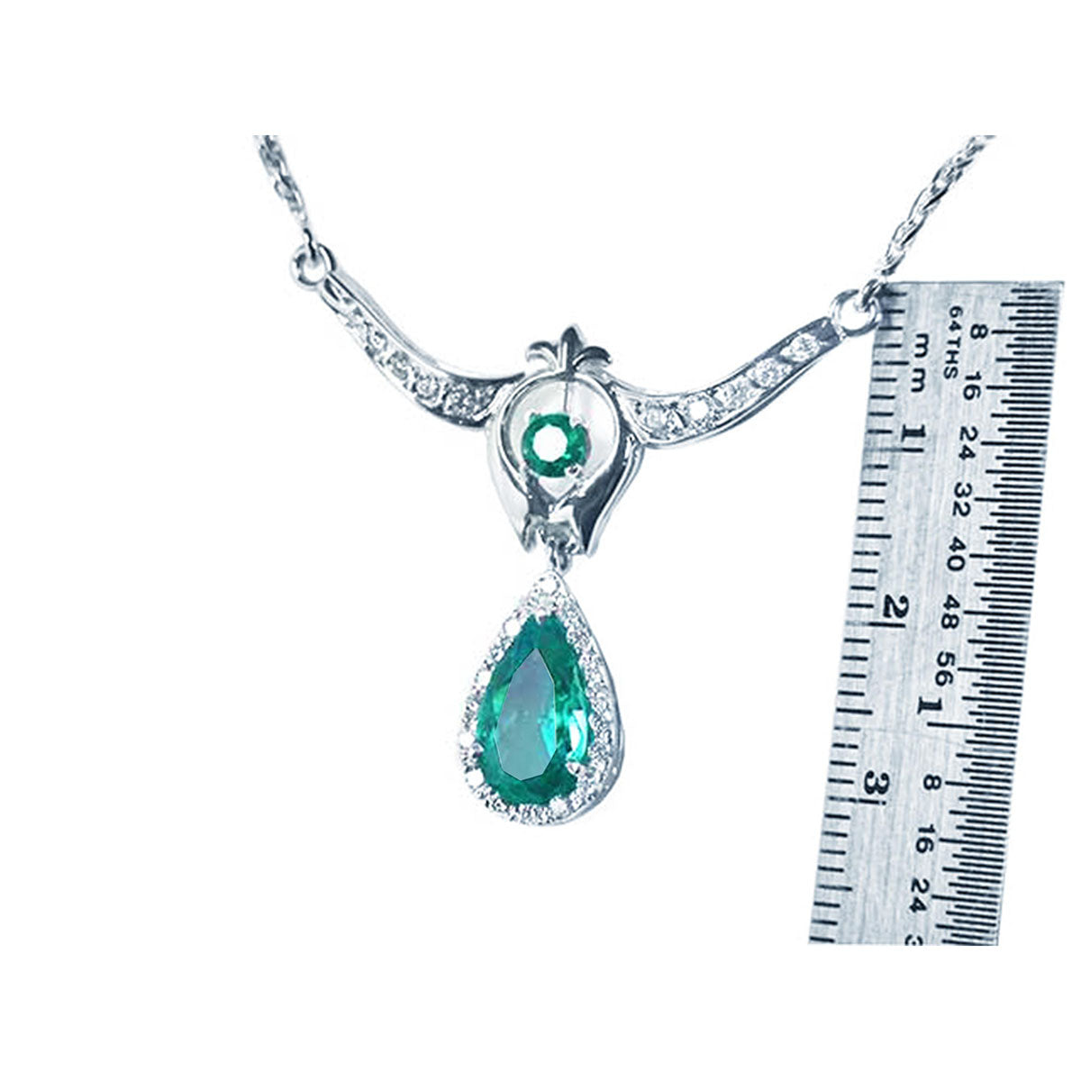 White gold emerald necklace with a green teardrop pendant next to a ruler for scale on a white background