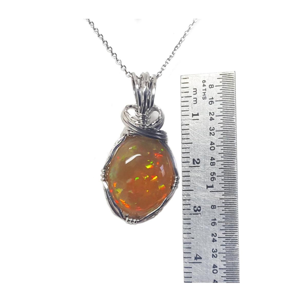 Opal pendant on a silver chain with a ruler for scale on a white background