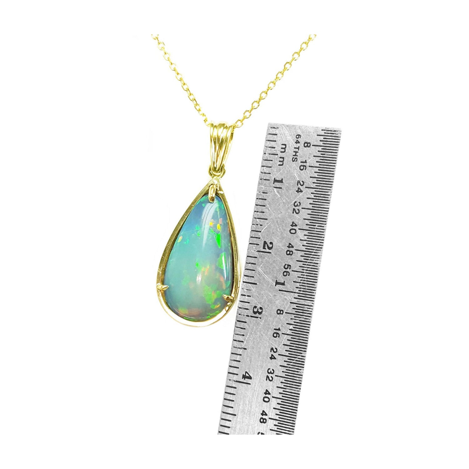 Opal pendant necklace with gold chain next to a ruler for scale on a white background