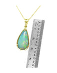 Opal pendant necklace with gold chain next to a ruler for scale on a white background