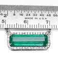 View of a natural elongated emerald gemstone pendant necklace with a halo diamond on a ruler for scale