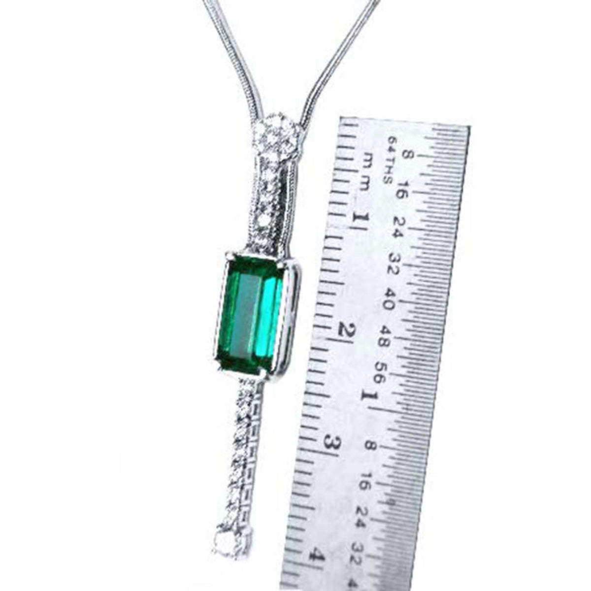 Necklace with a natural emerald gemstone and white gold chain next to a ruler for scale on a white background