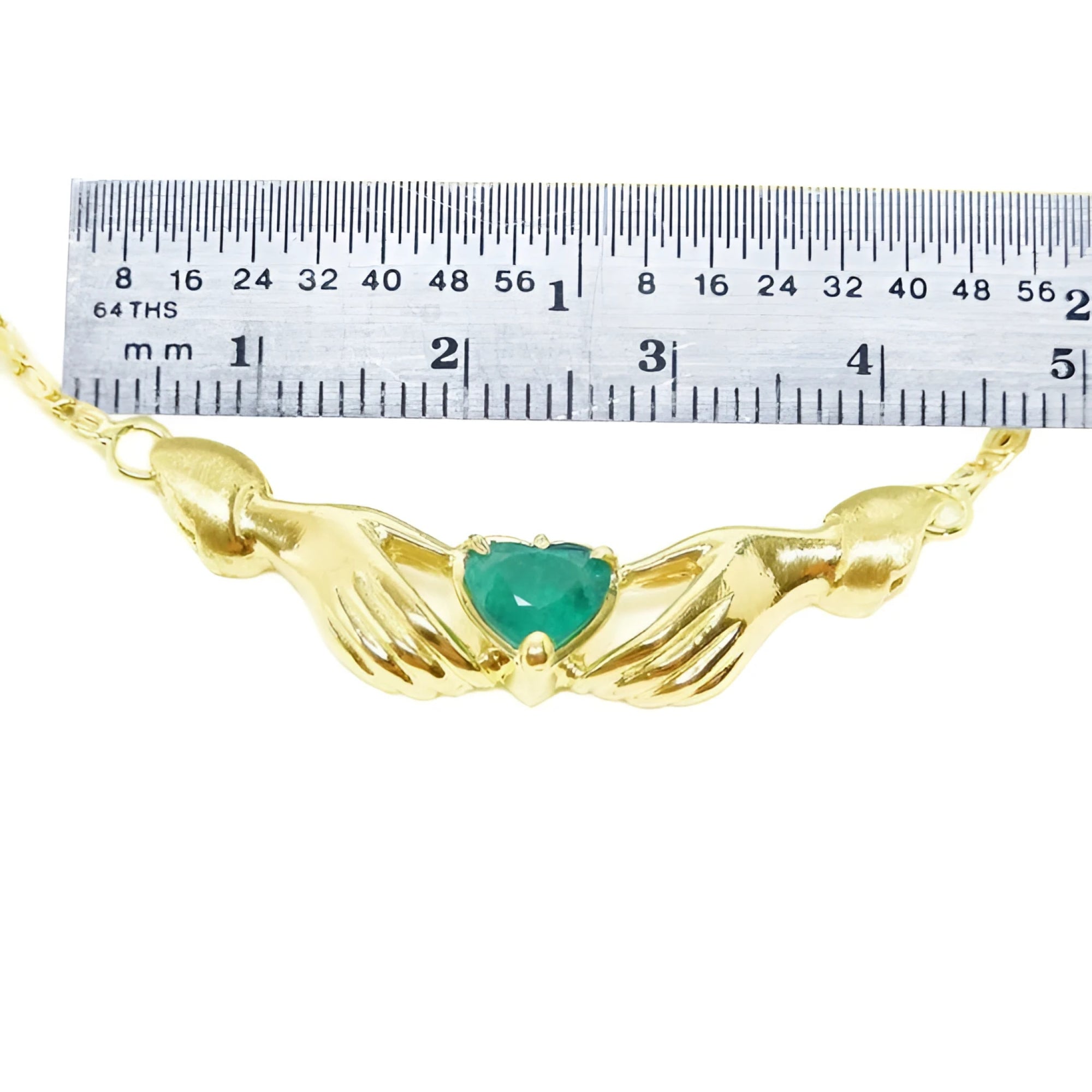 Emerald Claddagh necklace, heart-cut deep green emerald in 14K yellow gold, held by hands, with ruler for scale.
