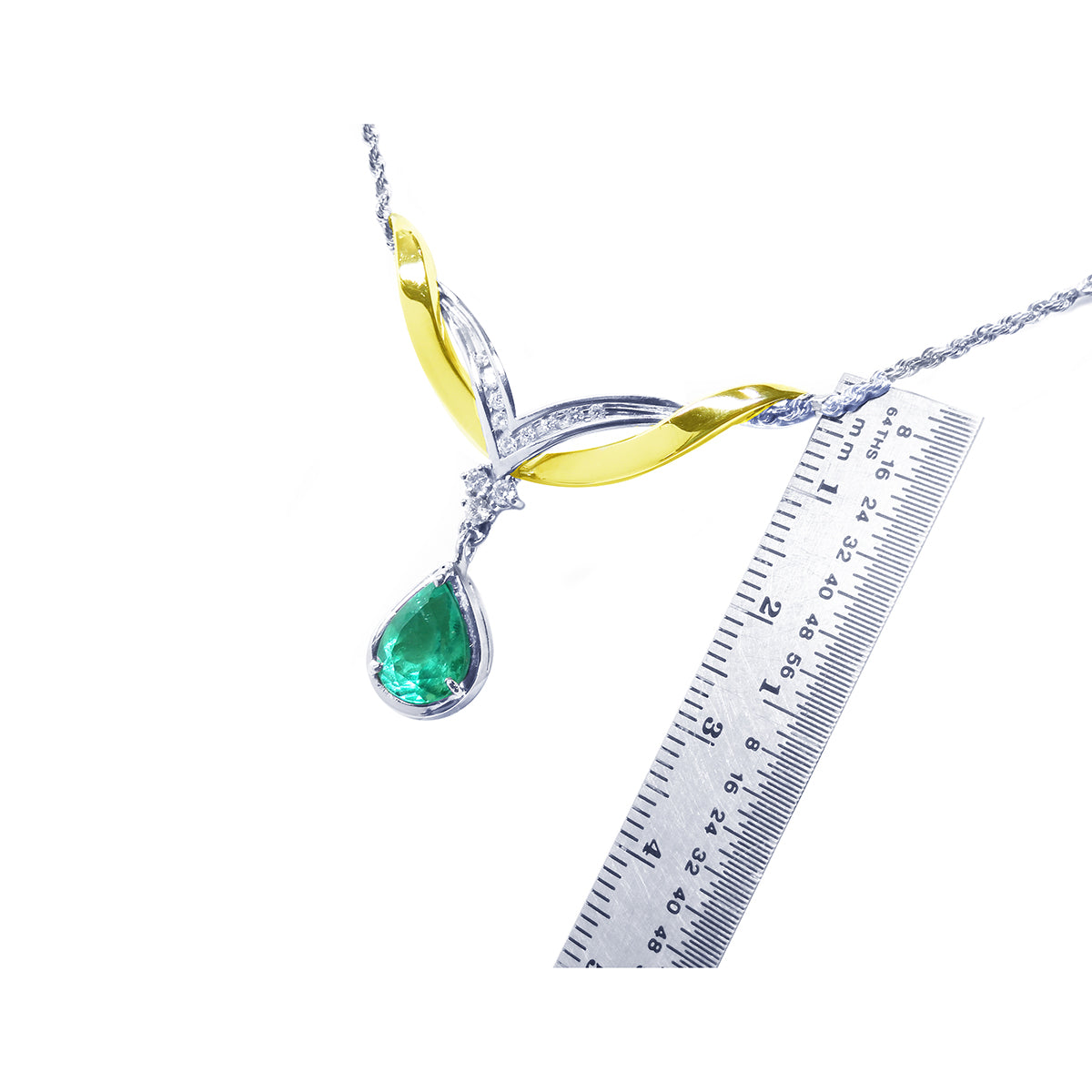 Jewelry with a teardrop natural emerald gemstone and gold accents next to a ruler for measuring size on a white background