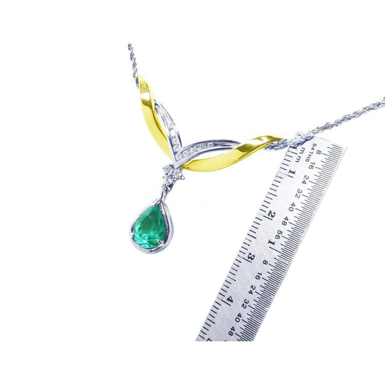 Jewelry with a teardrop natural emerald gemstone and gold accents next to a ruler for measuring size on a white background