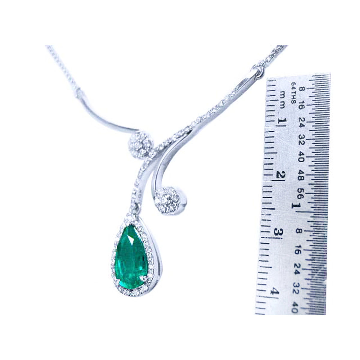 White gold necklace with a teardrop emerald gemstone pendant next to a ruler for scale on a white background