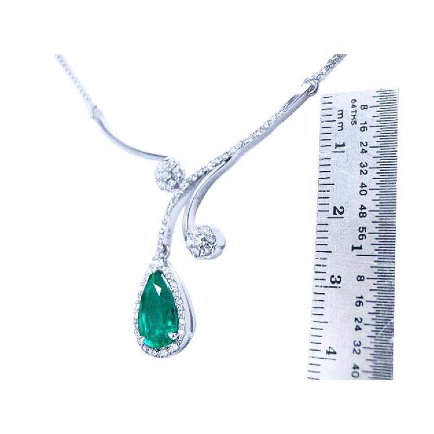 Pear cut 2.26ct natural emerald necklace in 18K white gold with diamond halo and accents, next to a ruler.