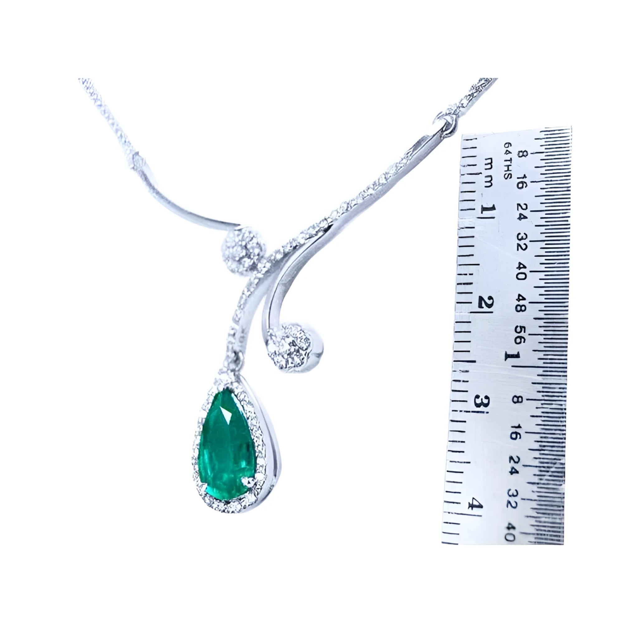 Pear cut 2.26ct natural emerald necklace in 18K white gold with diamond halo and accents, next to a ruler.