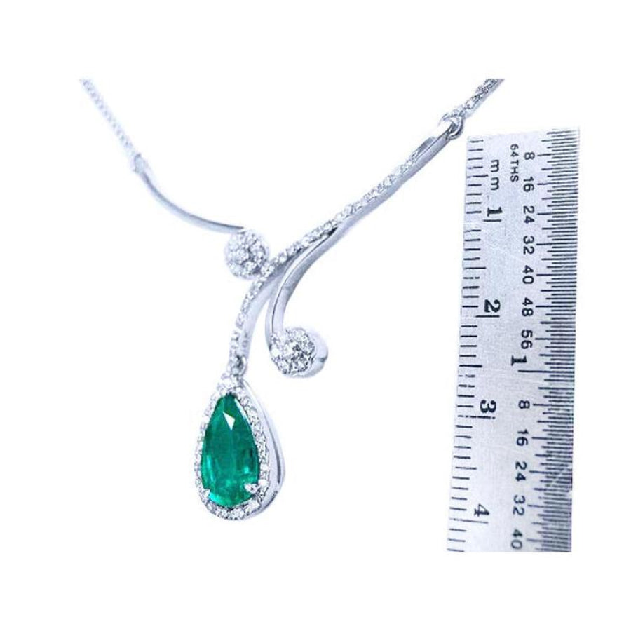 Pear cut 2.26ct natural emerald necklace in 18K white gold with diamond halo and accents, next to a ruler.