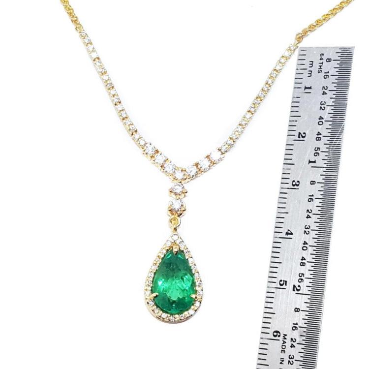 next to a ruler sizer of a genuine emerald necklace pear cut crafted in 18k yellow gold, halo diamond 