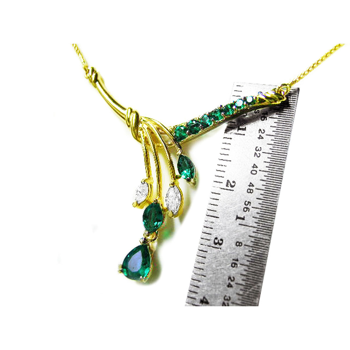 A yellow gold necklace with natural emeralds and diamonds gemstones next to a ruler on a white background