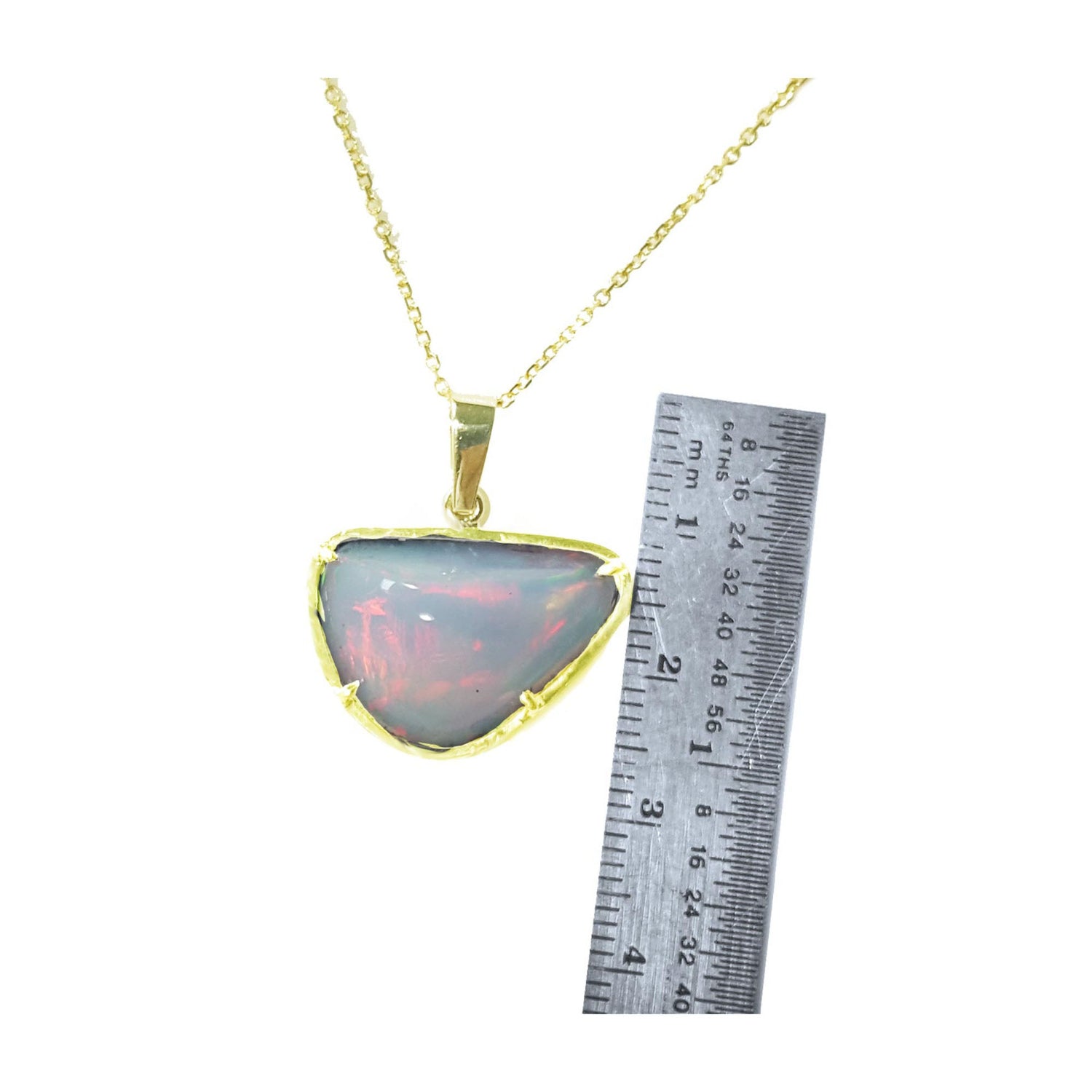 Opal pendant necklace with gold chain next to a ruler on a white background.