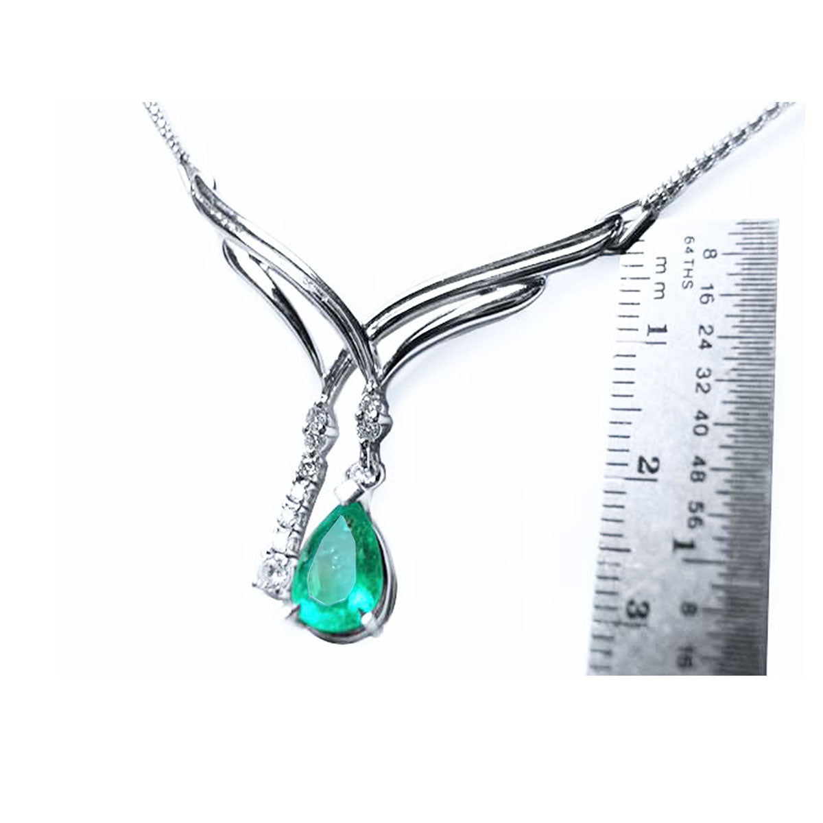 A 14k white gold emerald necklace natural pear cut with accent diamonds next to a ruler sizer