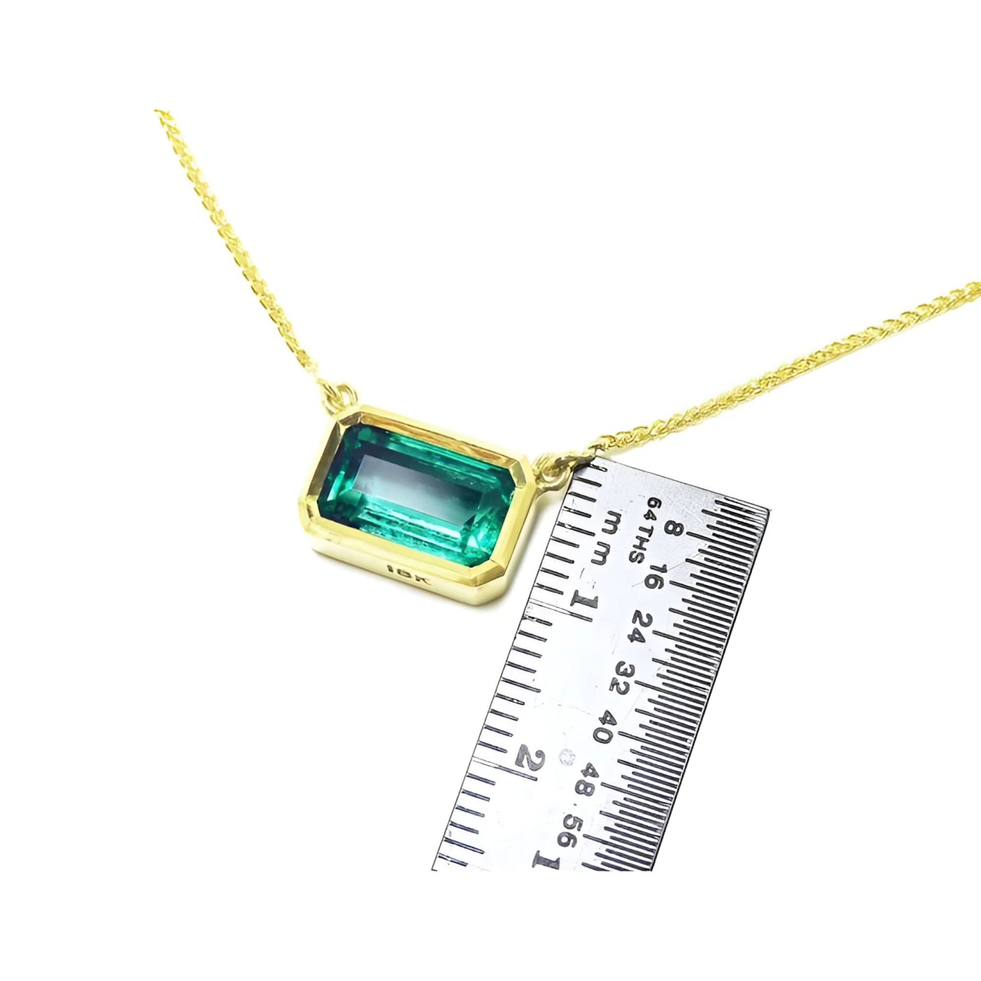 East-west emerald-cut solitaire emerald necklace in 18K yellow gold, shown with a ruler for scale.