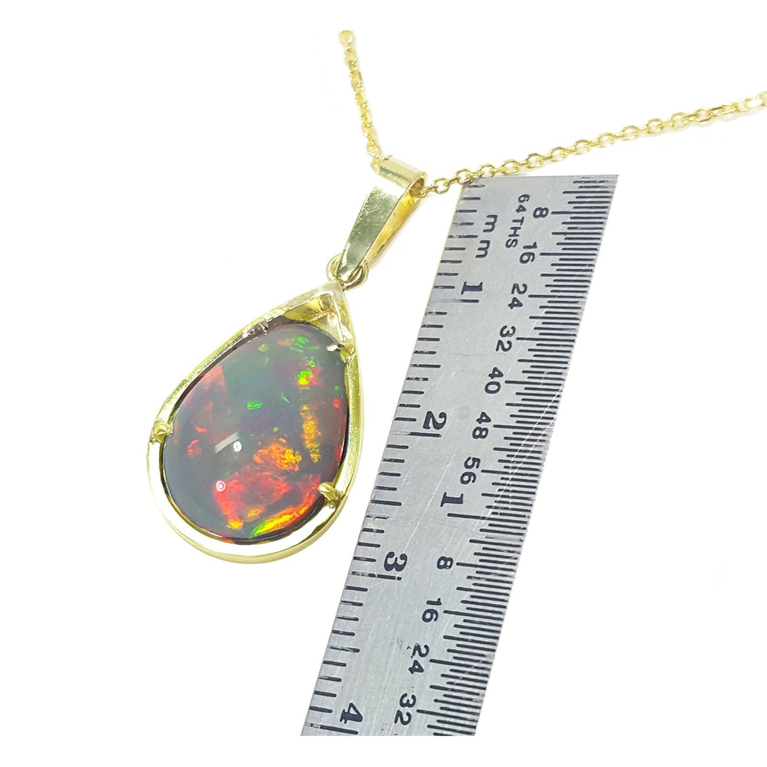 Opal pendant on a gold chain with a ruler for scale on a white background