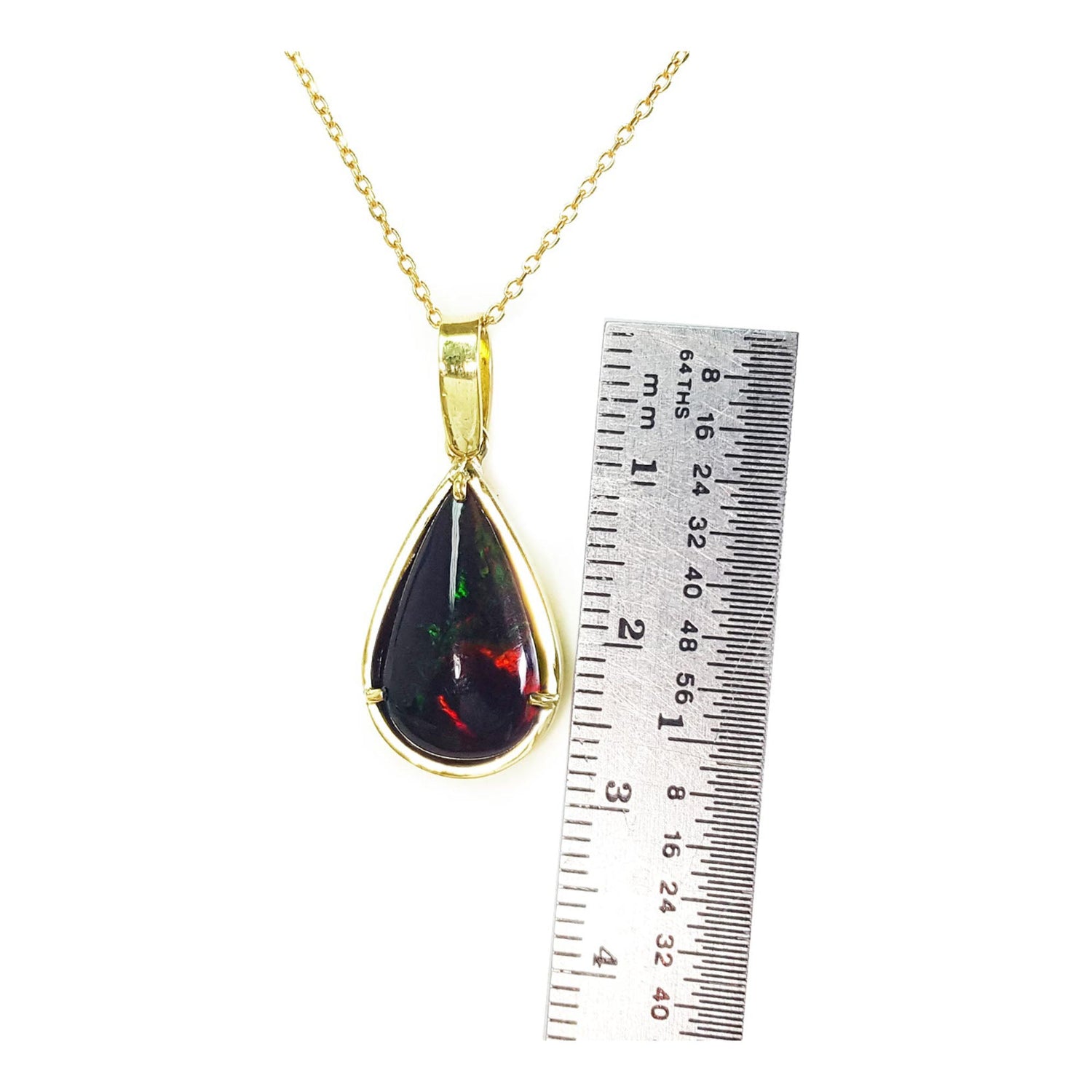 Teardrop-shaped pendant with gold chain and embedded red and green black opal, next to a ruler for scale.