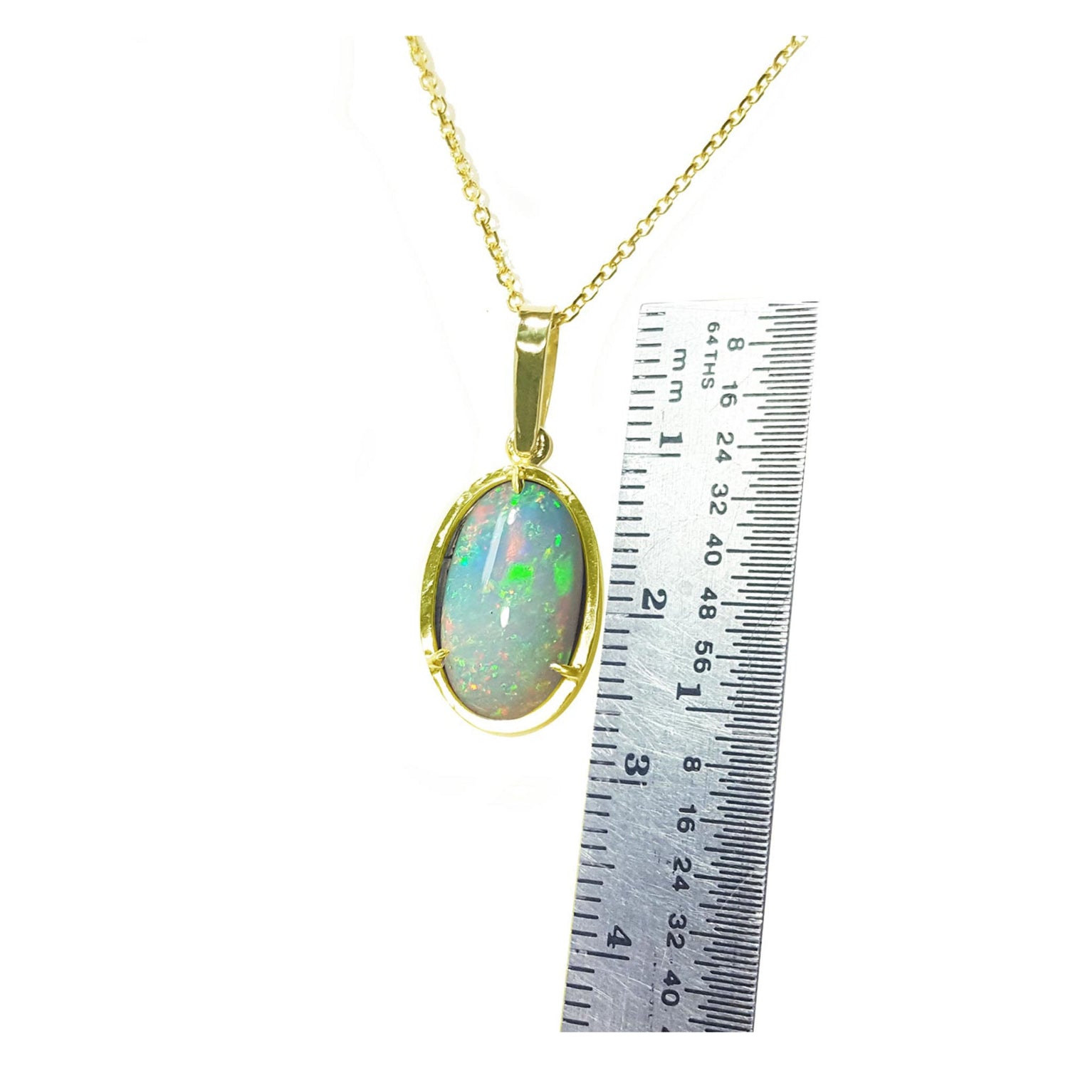 Opal pendant on a gold chain with a ruler for scale on a white background