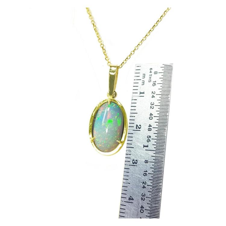 Oval Ethiopian opal pendant with bluish green hues, prong set in 14K yellow gold, shown next to a ruler.