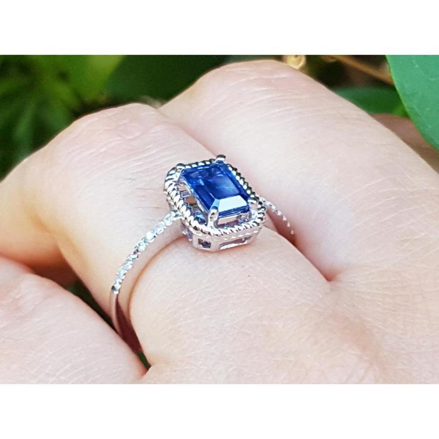 1.03 ct. emerald cut blue sapphire solitaire ring in 14K white gold with rope frame and accent diamonds.