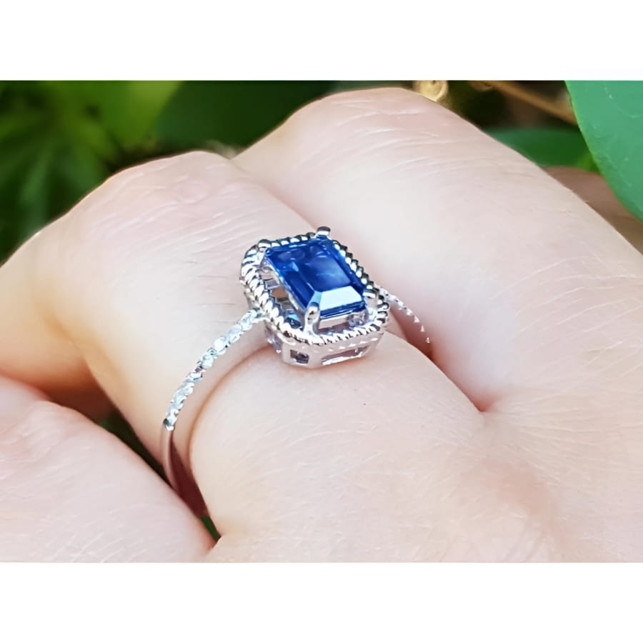 1.03 ct. emerald cut blue sapphire solitaire ring in 14K white gold with rope frame and accent diamonds.