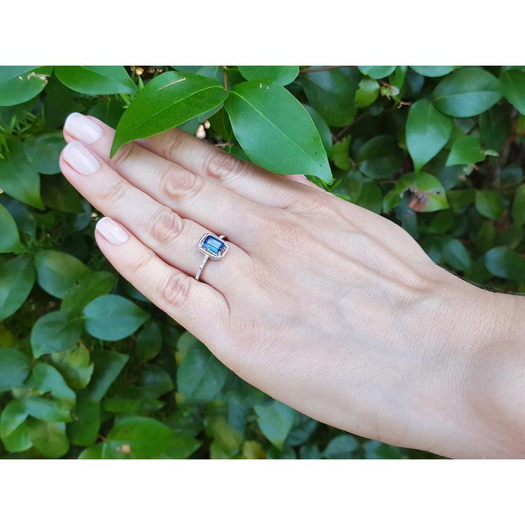 Hand wearing a 14k white gold ring with a blue natural sapphire against a green leafy background
