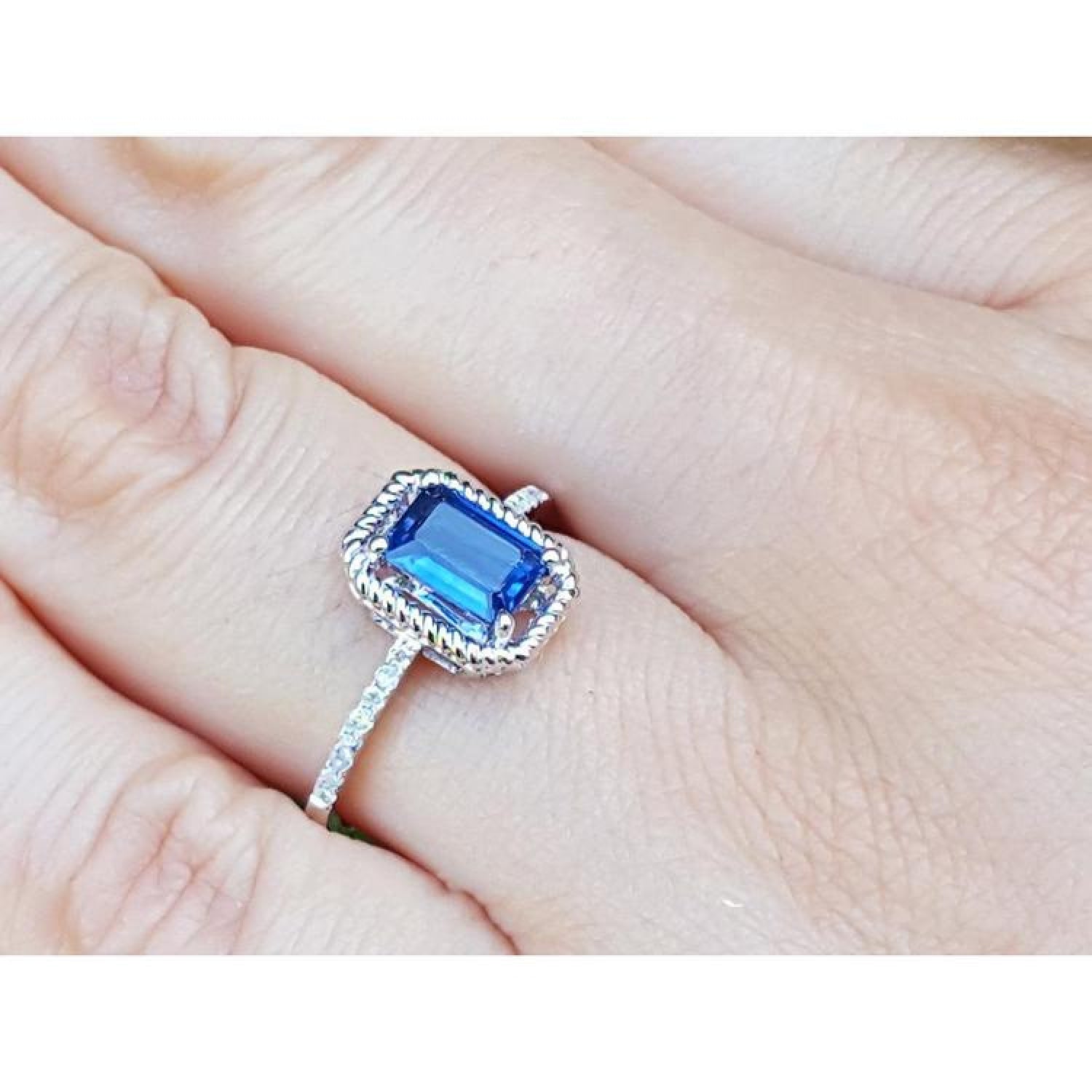 1.03 ct. emerald cut blue sapphire solitaire ring in 14K white gold with rope frame and accent diamonds.