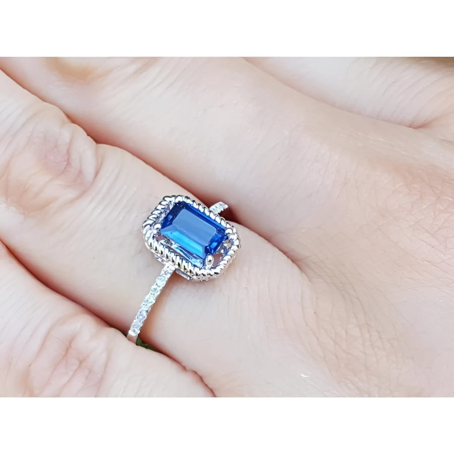 1.03 ct. emerald cut blue sapphire solitaire ring in 14K white gold with rope frame and accent diamonds.
