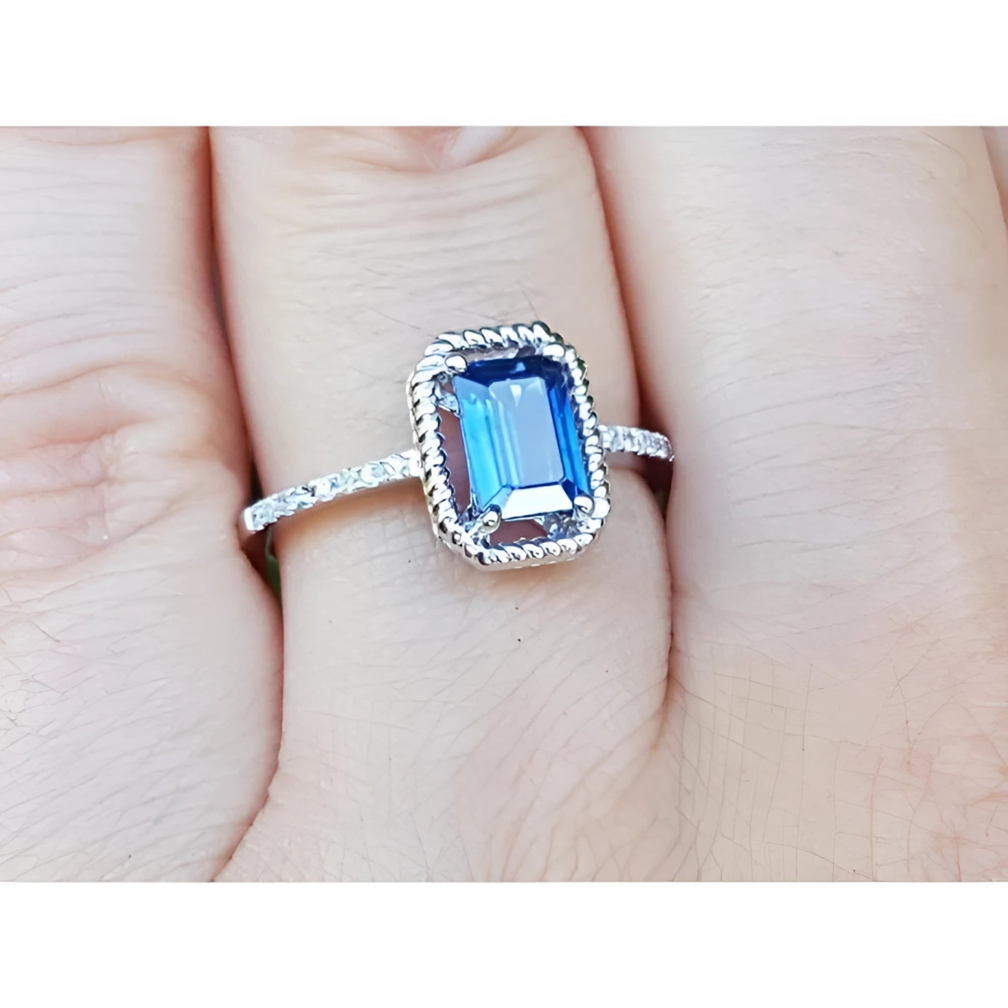 A women’s sapphire solitaire ring with a medium light blue stone, accented by diamonds, set in 14K white gold, shown on the finger.