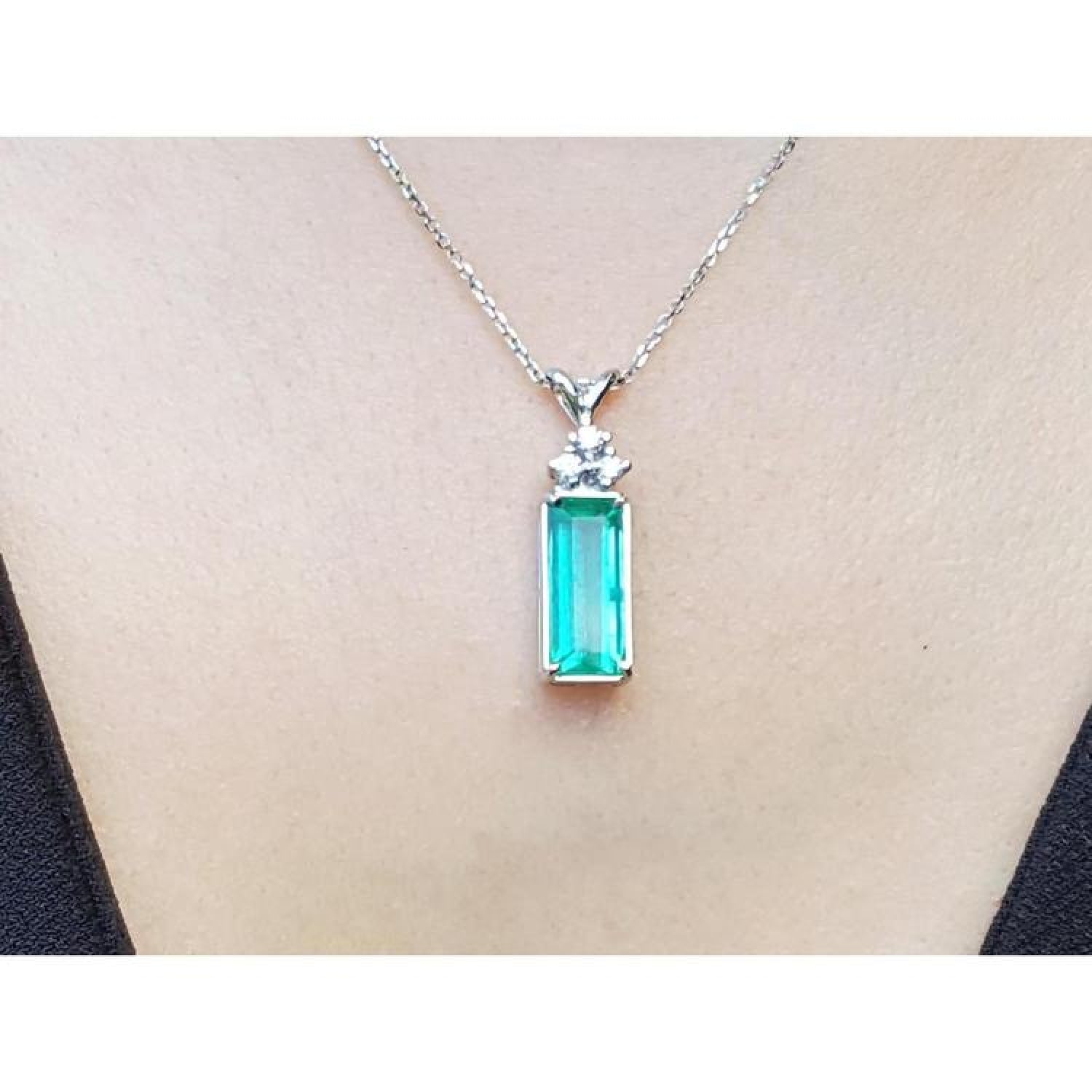 Emerald pendant with accent diamonds on a white gold chain, worn on a person's neck.