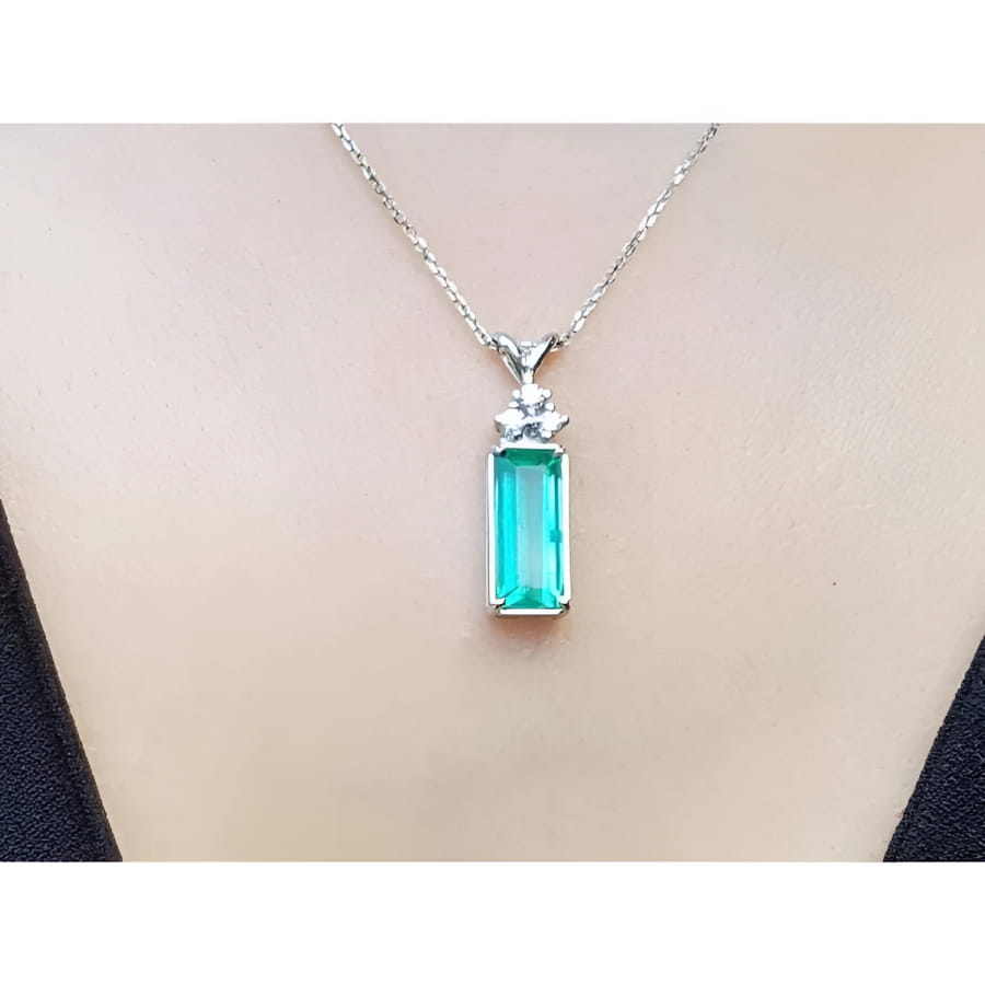 Emerald pendant with accent diamonds on a white gold chain, worn on a person's neck.