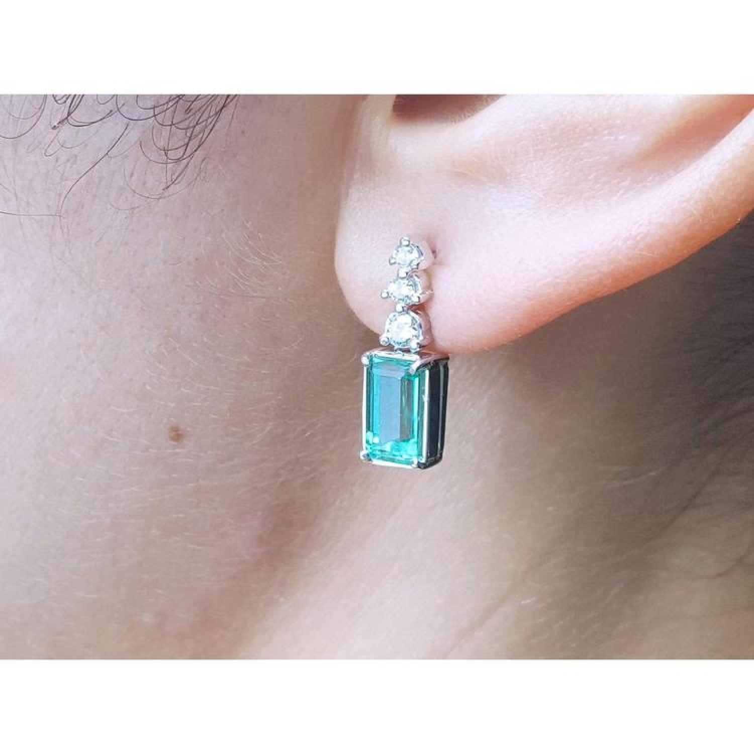 Emerald drop earring with three round diamonds in 14K white gold on an ear.
