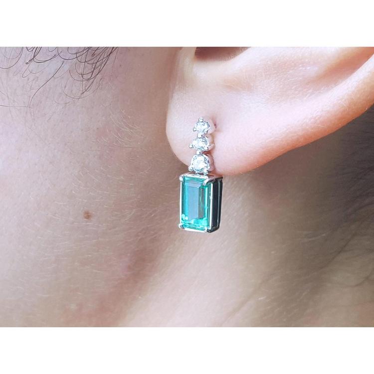 Close-up of a diamond earring with a natural emerald gemstone worn on an ear.