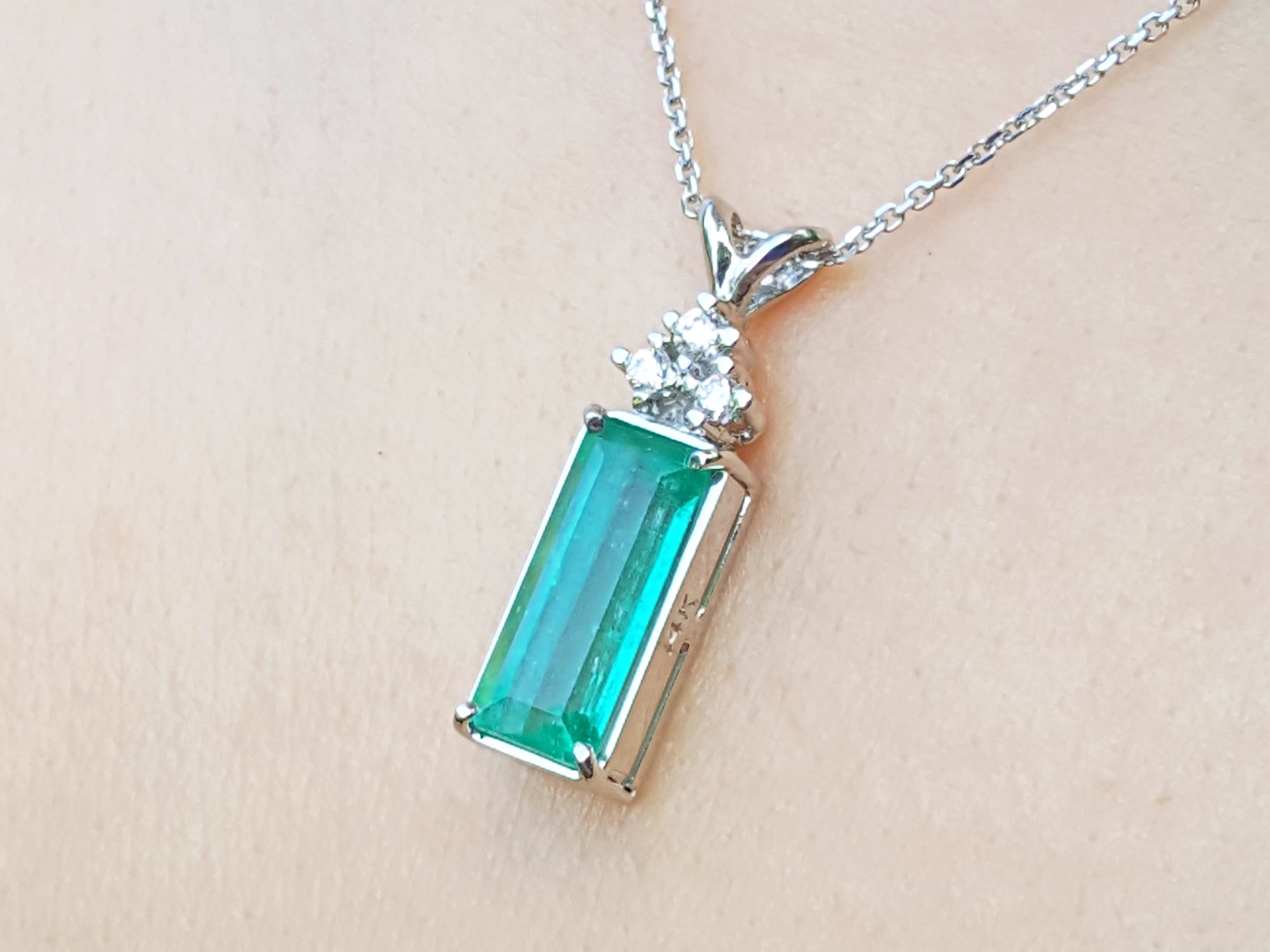 Emerald rectangular gemstone pendant with white gold chain on beige background