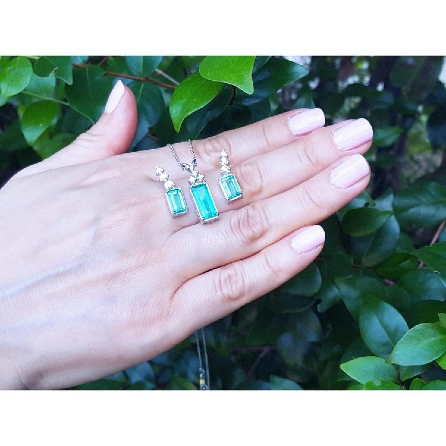 Emerald earrings and pendant set with diamonds in 14K white gold, held on a hand.