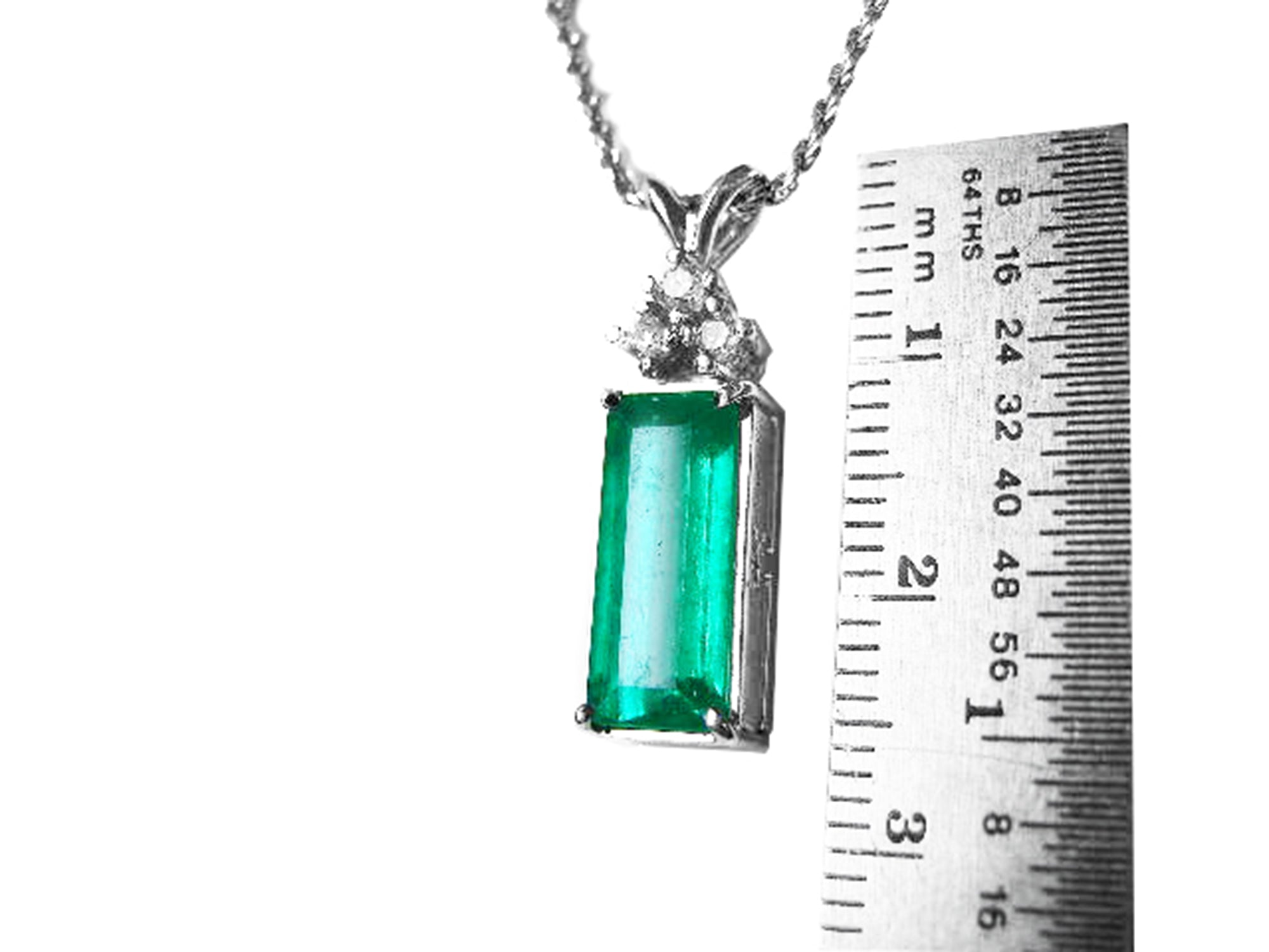A natural emerald pendant on a chain with a ruler for scale on a white background