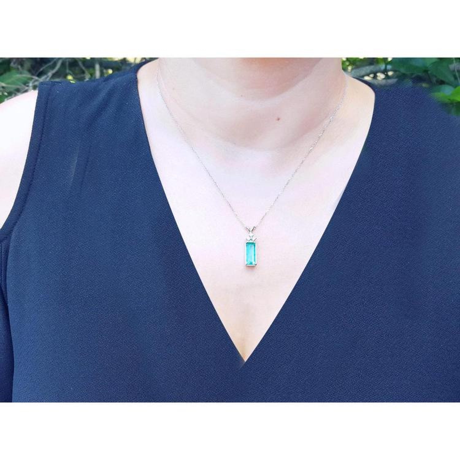 Emerald pendant with diamonds on a white gold chain, worn on a woman's neck.